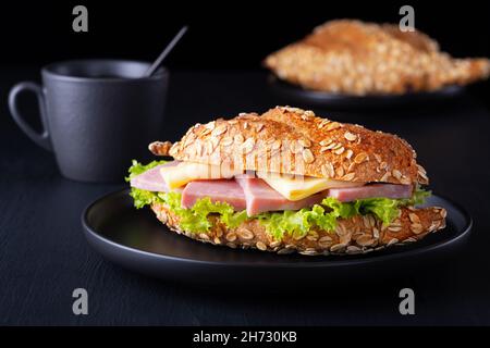 Croissant-Sandwich mit frischem Salat, Schinken und Frischkäse auf dunklem Hintergrund Stockfoto