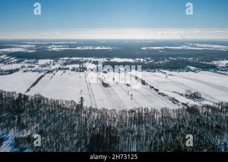 Winterlandschaft, Luftaufnahme des Waldes, schneebedeckte Felder und entferntes Dorf unter blauem Himmel Stockfoto