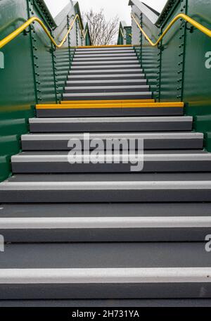 Treppenflucht an einem Bahnhof mit gelbem Rand und Geländern zur Unterstützung von behinderten und sehbehinderten Nutzern. Neue Eisenbahnbrücke mit Treppe. Stockfoto