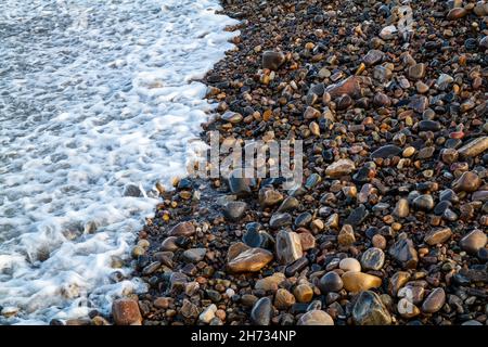 BUCKIE, MORAY, SCHOTTLAND - 19. NOVEMBER 2021: Dies ist eine sanfte Welle, die am 19. November 2021 auf den Kieselsteinen einer Küste in Buckie, Moray, Schottland, eintrifft Stockfoto