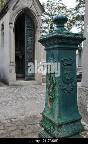 Auf einem Pfad in der Nähe eines Mausoleums auf dem historischen Friedhof Passy (Cimetière de Passy) in Paris steht ein gusseiserner Brunnen. Stockfoto