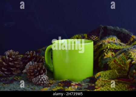 Grüner Becher, Tannenzapfen und eine warme Decke im dunklen Hintergrund Stockfoto