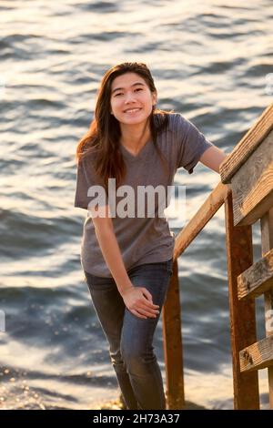 Biracial asiatische Teenager-Mädchen auf Steinstufen, die hinunter zum Wasser Stockfoto