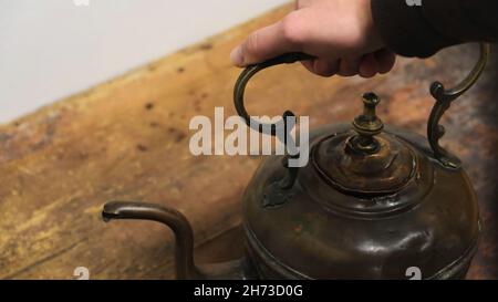 Nahaufnahme der Hand eines Mannes, der einen alten Eisenkessel vom Holzbrett nahm. Ausstellung im Museum Stockfoto