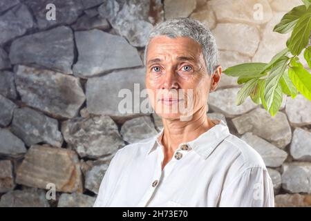 Porträt der glücklichen älteren Frau in der Nähe des Steinzauns Stockfoto