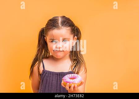 Kind Mädchen holdind auf der Hand ein rosa Donut. Auf einem gelben Hintergrund Stockfoto