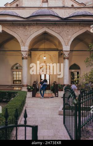 SARAJEVO, BOSNIEN UND HERZEGOWINA - 16. Sep 2021: Eine vertikale Aufnahme von Menschen, die die Gazi-Husrev-Beg-Moschee nach Maghrib betreten, dem Abendgebet in Saraj Stockfoto
