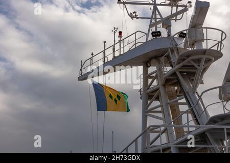 Low-Angle-Aufnahme der Flagge von St. Vincent und den Grenadinen, die im Wind auf dem Mast des Schiffes winken. Blauer wolkig Himmel als Hintergrund. Stockfoto