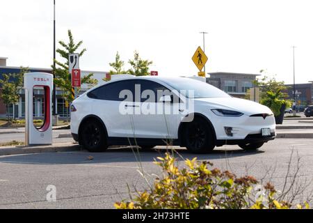 Ein weißer Tesla Model X parkte an einem sonnigen Tag an einer Tesla Supercharger-Netzwerkstation in einem städtischen Gebiet. Stockfoto