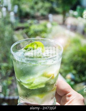 Ein erfrischender Mojito-Drink in der Hand einer Frau. Vertikal, im Freien, an einem sonnigen Sommertag Stockfoto