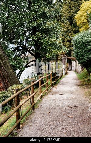 Holzzaun entlang des Weges im grünen Garten. Villa Monastero, Italien Stockfoto