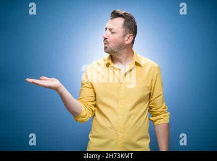 Seitenansicht von schönen jungen Mann senden Kuss auf Sie über blauen Hintergrund, Kleider in gelbem Hemd. Hübsch schönen Kerl küssen und zeigt ihre Handfläche, Kopie s Stockfoto