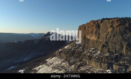 Landschaft von schneebedeckten Klippen an einem suny Tag auf blauem Himmel Hintergrund. Luftaufnahme der steilen Klippen und grünen dichten Wald an ihren Hängen und Stockfoto