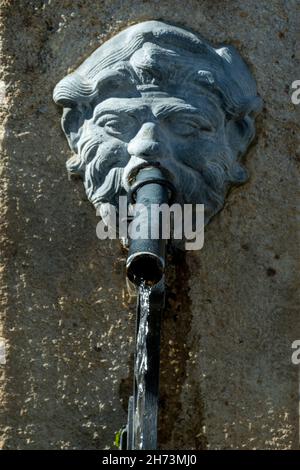 Dekorativer Steinbrunnen mit Löwenkopf, der an einer rustikalen Wand angebracht ist Stockfoto