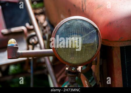 Nahaufnahme eines Oldtimer-Traktorscheinwerfers auf einem Bauernhof während des Tages mit rustikalen Landmaschinen Stockfoto