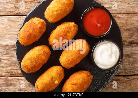 Croquetas de Bacalao Cod Kroketten mit Saucen schließen sich in der Schieferplatte auf dem Tisch an. Horizontale Draufsicht von oben Stockfoto