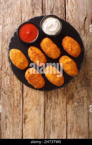 Croquetas de Bacalao Spanish Salt Cod Tapas mit Saucen in der Schieferteller auf dem Tisch schließen. Vertikale Draufsicht von oben Stockfoto