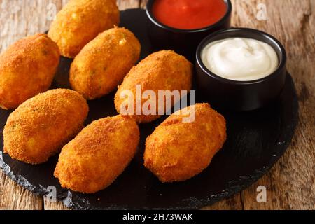 Spanische Kroketten mit gesalzenem Kabeljau, serviert mit Soßen aus der Nähe auf einem Schieferteller auf dem Tisch. Horizontal Stockfoto