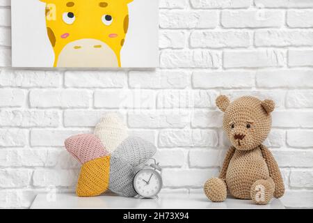 Teddybär-Spielzeug mit Kissen und Wecker auf dem Tisch in der Nähe der Ziegelwand Stockfoto