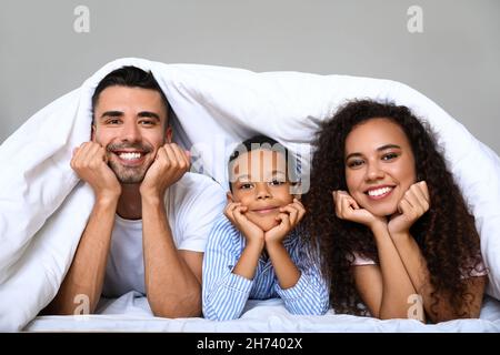 Glückliche interrassische Familie, die unter der Decke im Bett lag Stockfoto