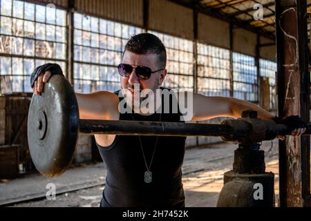 Arbeiter in einer Fabrik am Metallbieger, der Metallstange mit Schutzhandschuhen an einer Presse zusammenklemmend. Altmodische Spannvorrichtung aus Metall. Stockfoto
