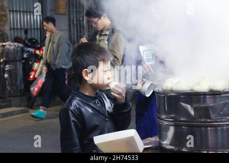 Junge, die traditionelle chinesische Dampfbrötchen beim Essen auf der Straße essen Stockfoto