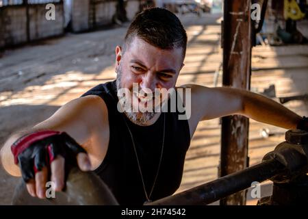 Arbeiter in einer Fabrik am Metallbieger, der Metallstange mit Schutzhandschuhen an einer Presse zusammenklemmend. Altmodische Spannvorrichtung aus Metall. Stockfoto