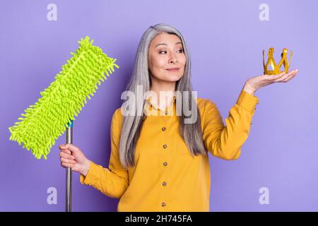 Portrait von attraktiven fröhlich stolze Frau hält Tiara Boden Mopp Waschmaschine Reinigung isoliert auf hellen violett lila Farbe Hintergrund Stockfoto