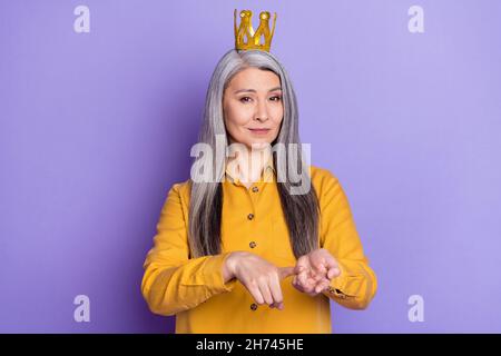 Portrait einer attraktiven strengen Frau, die Krone trägt und sich auf einem hellen violett-violetten Hintergrund vortäuscht Stockfoto