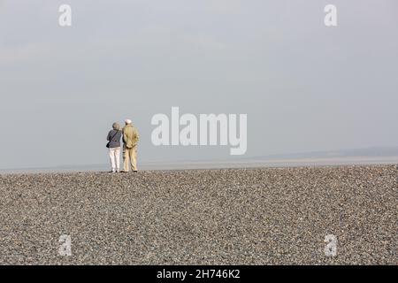 Paar am Rande eines Kiesstrandes beobachten das Meer. Plage du Hourdel, Baie de Somme, Frankreich Stockfoto