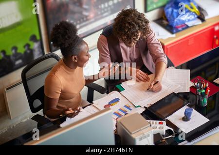 Draufsicht auf zwei Kollegen, männlich und weiblich, kaukasisch und afroamerikanisch, die im Amt an statistischen Daten arbeiten Stockfoto