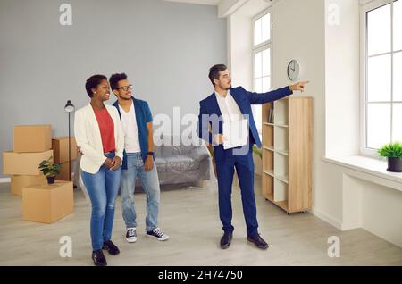 Männliche makler zeigt jungen Paar schöne Aussicht vom Fenster in neue geräumige Wohnung. Stockfoto