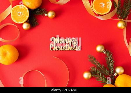 Die Inschrift Merry christmas auf rotem Hintergrund ist mit Weihnachtsschmuck, Bändern, Mandarinen und Nadelzweigen geschmückt. Weihnachten ca. Stockfoto