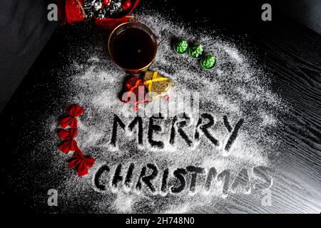 Fröhliche Weihnachten schreiben in den gefälschten Schnee auf den Tisch mit Tasse Kaffee und jingle Glocken Stockfoto
