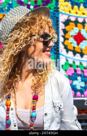 Porträt von glücklichen erwachsenen Frau mit blonden langen lockigen Haaren und Mode-Stil lächeln und genießen Sie Freizeit im Freien. Farbenfroher Hintergrund und fröhliche fema Stockfoto