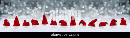 Breite Panorama-Reihe von rot weißen Plüsch weihnachtsmann weihnachtsmütze auf Schnee vor silbergrauen Bokeh Lichter Hintergrund Stockfoto