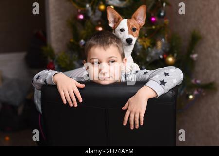 Ein Junge mit einem Hund Jack Russell auf dem Hintergrund eines Weihnachtsbaums. Stockfoto