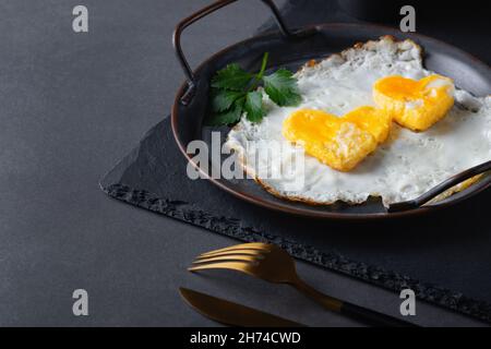 Hausgemachtes Spiegelei in einer Vintage-Pfanne auf grauem Hintergrund. Herzförmiges Eigelb. Platz für Text kopieren Stockfoto