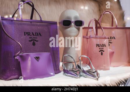 Lila und rosa Damen-Handtaschen, Sonnenbrillen und silberne High Heels in einem luxuriösen Schaufenster der italienischen Luxusmodemarke Prada Stockfoto