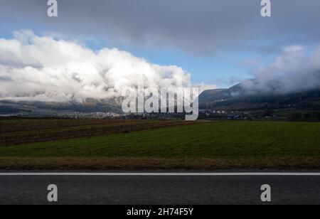 Eine Aufnahme aus dem Fahrerfenster eines Elektroautos mit schneebedeckten alpen-Bergen. Kalter, wolkiger Herbsttag. POV erste Person Ansicht auf einem geschossen Stockfoto