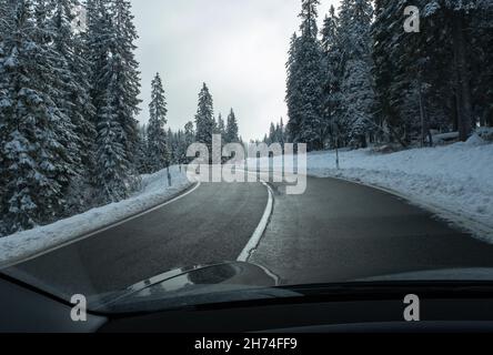 Ein Schuss auf die Bewegung hinter der Windschutzscheibe eines Elektroautos mit schneebedeckten alpen-Bergen. Kalter, wolkiger Herbsttag. POV-Ansicht der ersten Person aufgenommen Stockfoto