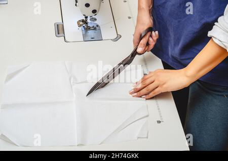 Vintage Schneiderschere geschnitten weißen Stoff. Frauenhände. Stockfoto