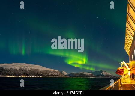 Unterwegs mit dem Postschiff nach Tromsø, Nordlichter über den schneebedeckten Lyngenalps. Aurora Borealis, Norwegen. Rettungsboot am Kreuzfahrtschiff Stockfoto