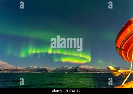 Unterwegs mit dem Postschiff nach Tromsø, Nordlichter über den schneebedeckten Lyngenalps. Aurora Borealis, Norwegen. Rettungsboot am Kreuzfahrtschiff Stockfoto