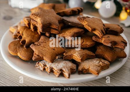 Teilweise verschwommener Teller mit Lebkuchenkuchen in Form von weihnachtsbäumen, Sternen und Herzen stehen auf der Küchenarbeitsplatte vor christm-Hintergrund Stockfoto