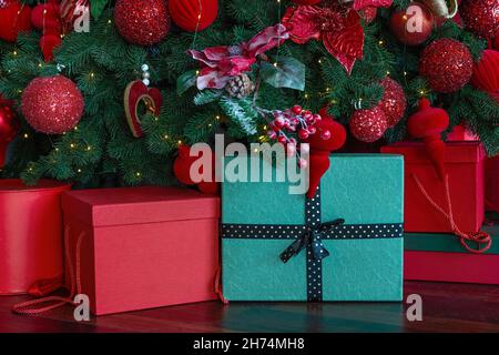 Weihnachten, Feiertage, Geschenke, Neujahr und Feiertagskonzept. Nahaufnahme von roten und grünen Geschenkschachteln unter Dekoration Weihnachtsbaum auf Holzboden. Selektiver Fokus Stockfoto