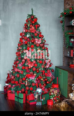 Weihnachtsbaum mit roten und grünen Kugeln, Spielzeug und Ornaten in einem dunklen Innenraum geschmückt. Tannenbaum aus dem neuen Jahr, geschmückt mit Geschenken und hellen Schachteln. Vertikale Aufnahme Stockfoto