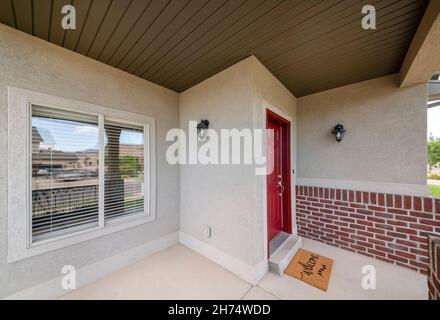 Veranda eines Hauses mit kastanienbraunen Eingangstür und gelber Fußmatte Stockfoto