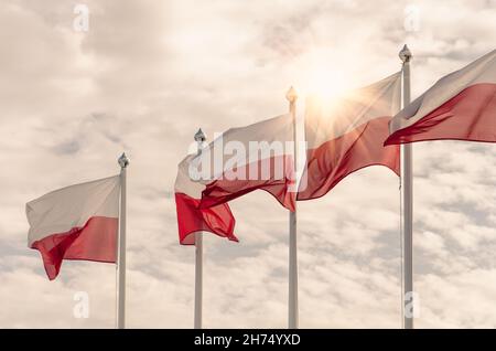 Polnische Nationalflaggen flattern im Wind auf einem wolkigen Hintergrund mit Sonnenstrahlen Stockfoto