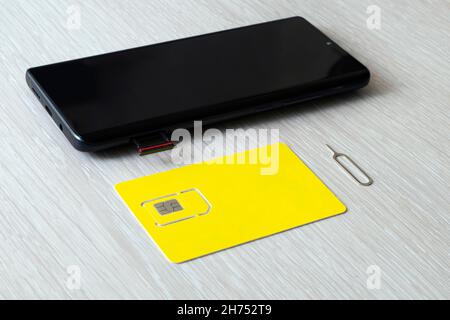 SIM-Karte und microSD-Kartenfach mit Ausbauwerkzeug an der Seite des Smartphones auf einem Holztisch. Freier Platz für Design und Text Stockfoto